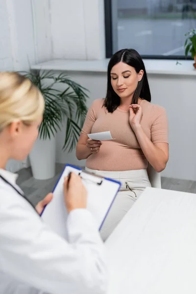 Flou médecin écriture prescription sur presse-papiers près de la femme enceinte — Photo de stock