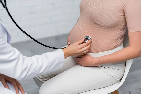 Partial view of pregnant woman near doctor examining her tummy with stethoscope — Stock Photo