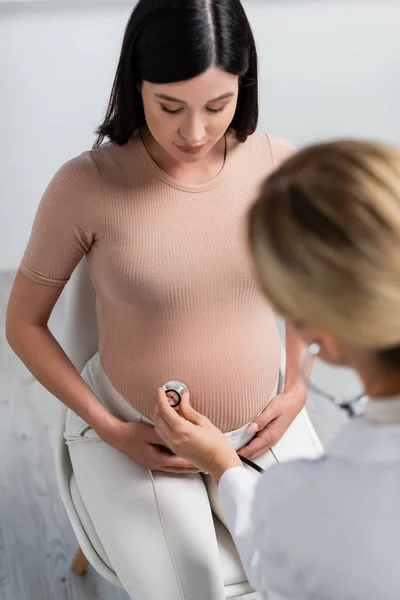 Размытый доктор осматривает животик беременной женщины в консультационной — стоковое фото