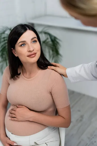 Médico desfocado tocando ombro de mulher grávida positiva na clínica — Fotografia de Stock