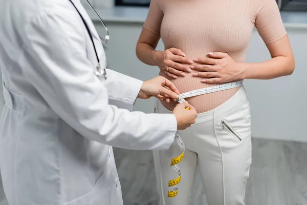 Vista recortada de la mujer embarazada cerca del médico midiendo su vientre en la clínica - foto de stock