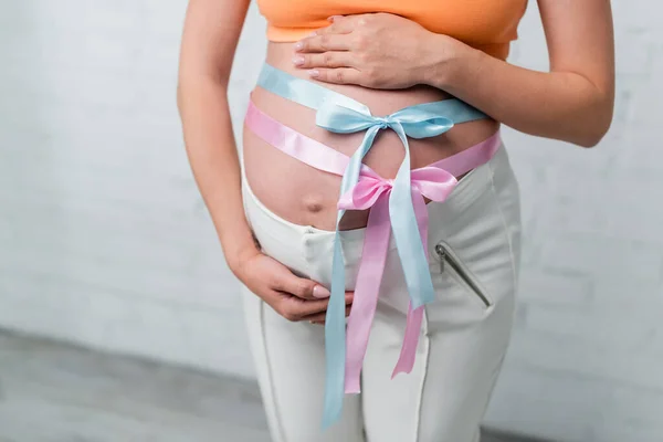 Vista parcial de la mujer embarazada con cintas de satén y arcos en el vientre — Stock Photo