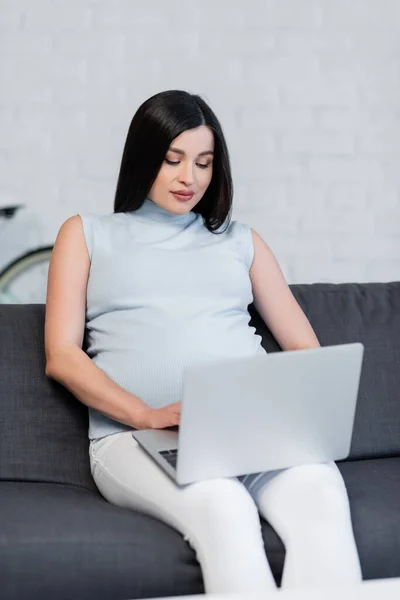 Young pregnant woman using computer on couch in living room — Stock Photo