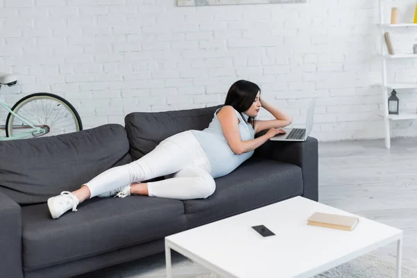 Full length view of pregnant woman using laptop on sofa in living room — Stock Photo