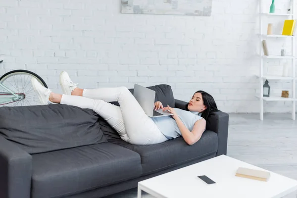 Pregnant woman typing on laptop while lying on couch in living room — Stock Photo