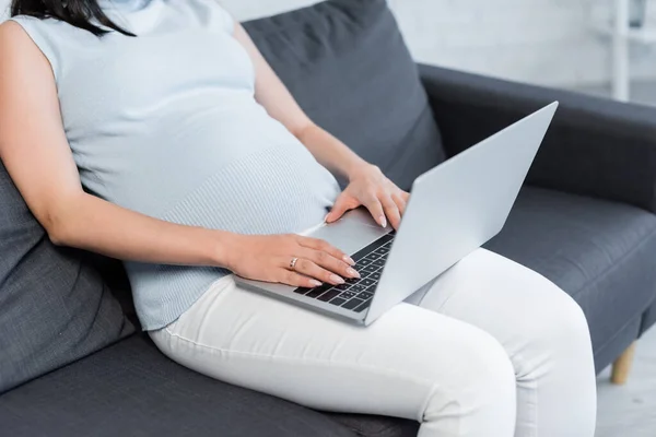 Teilbild einer schwangeren Frau, die zu Hause auf dem Sofa am Laptop arbeitet — Stockfoto
