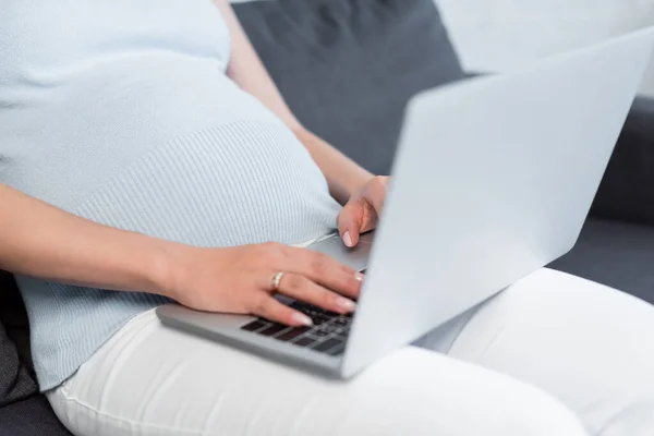 Обрезанный вид беременной женщины, печатающей на размытом ноутбуке дома — стоковое фото