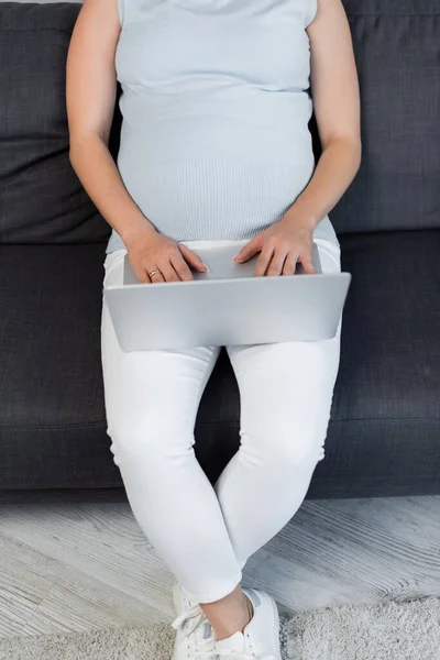 Vista cortada da mulher grávida trabalhando no laptop no sofá em casa — Fotografia de Stock