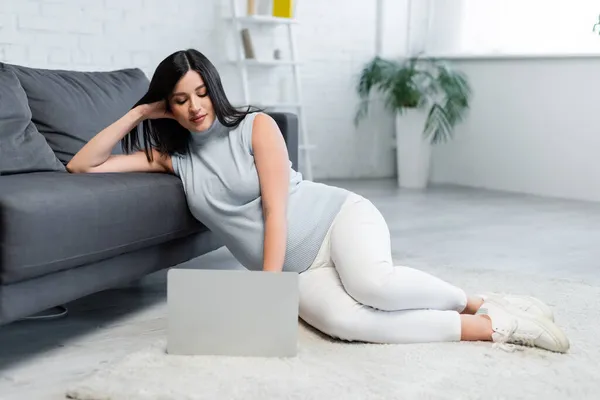 Comprimento total da mulher grávida usando laptop enquanto sentado no tapete de chão perto do sofá — Fotografia de Stock