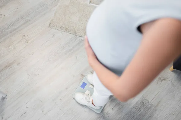 Ausgeschnittene Ansicht einer schwangeren Frau, die zu Hause auf einer Bodenwaage steht — Stockfoto