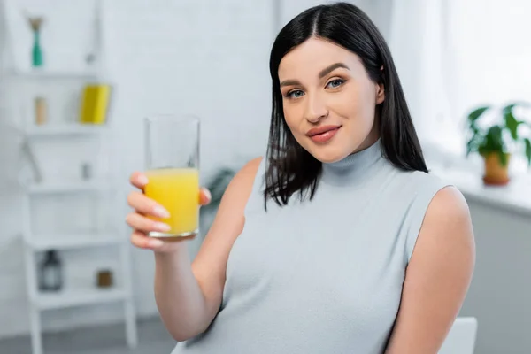 Young woman looking at camera while holding glass of fresh orange juice — Stock Photo