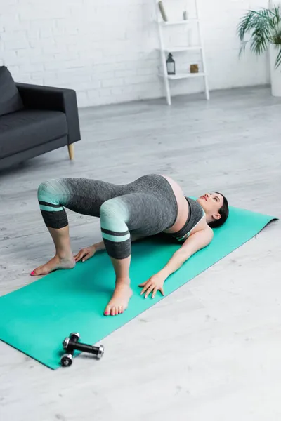 Joven embarazada ejercicio en puente pose en yoga mat en casa - foto de stock