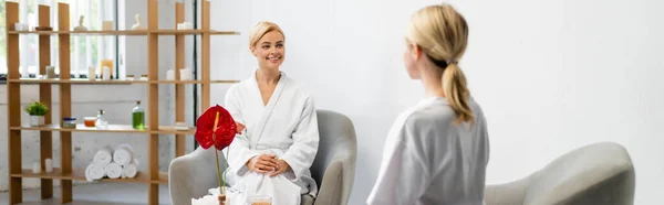 Mujer feliz en albornoz mirando especialista en spa borrosa, pancarta - foto de stock