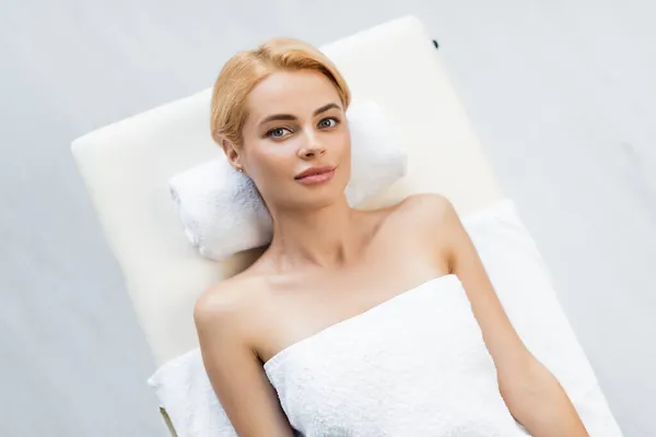 Vista superior de la mujer rubia con los hombros desnudos acostado en la mesa de masaje en el centro de spa - foto de stock