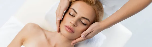 Top view of masseur doing face massage of blonde client with closed eyes, banner — Stock Photo