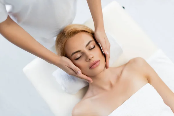 Top view of masseur doing face massage of blonde client with closed eyes — Stock Photo
