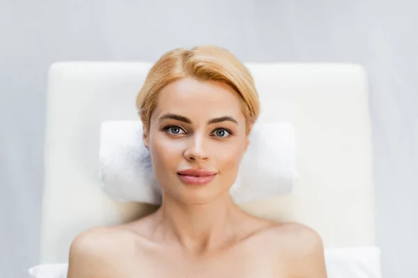 Top view of blonde client with bare shoulders lying on massage table in spa center — Stock Photo