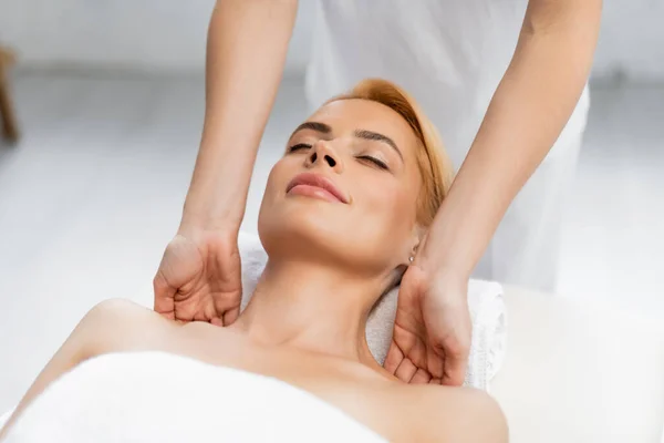 Blonde client with closed eyes receiving shoulder massage in spa center — Stock Photo