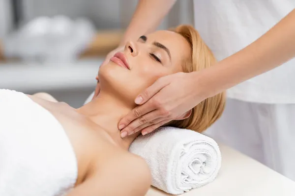 Cliente rubio con los ojos cerrados recibiendo masaje de cuello en el centro de spa - foto de stock