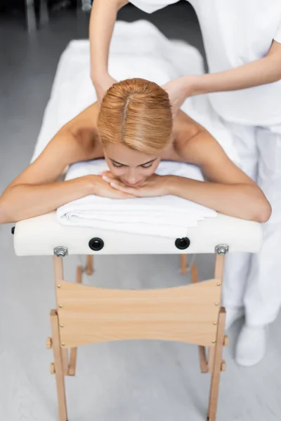 Massagista fazendo massagem nas costas para cliente loiro com olhos fechados — Fotografia de Stock