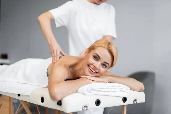 Массажист, делающий массаж плеч улыбающемуся клиенту в спа-центре — стоковое фото