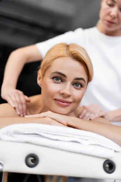 Blurred masseur doing shoulder massage to pleased client in spa center — Stock Photo