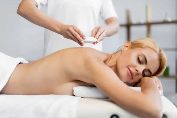 Masseur placing hot stone on blonde client in spa center — Stock Photo