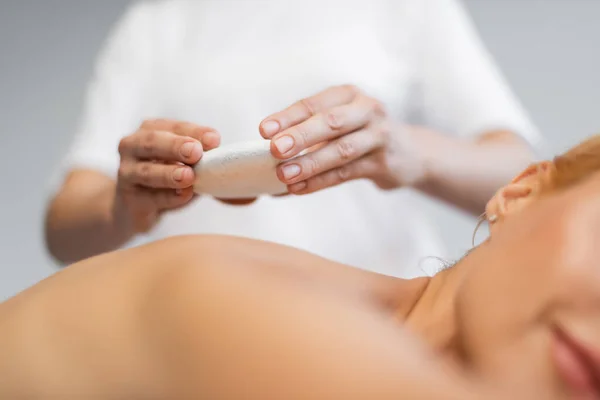 Cropped view of blurred masseur placing hot stone on body of client in spa center — Stock Photo