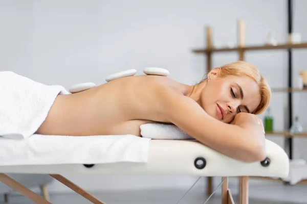 Blonde woman with closed eyes receiving hot stone massage in spa center — Stock Photo