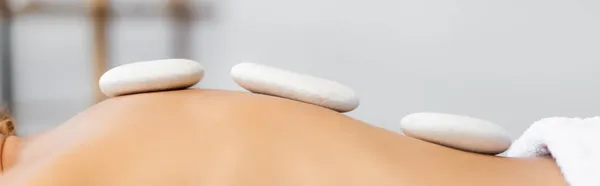 Обрізаний вид жінки, що отримує масаж гарячим каменем у спа-центрі, банер — стокове фото