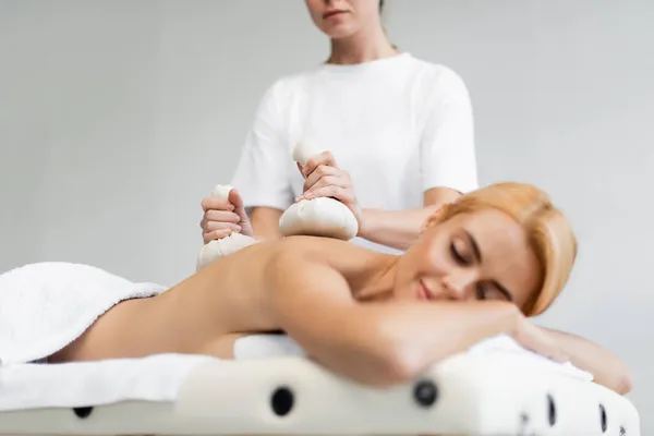 Blonde woman with closed eyes receiving massage with herbal bags in spa center — Stock Photo