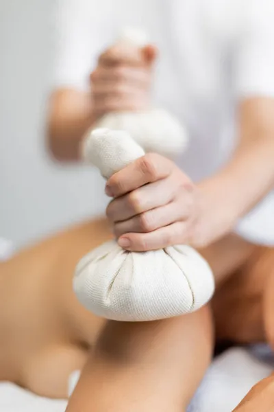 Partial view of masseur holding herbal bag while doing massage to client — Stock Photo