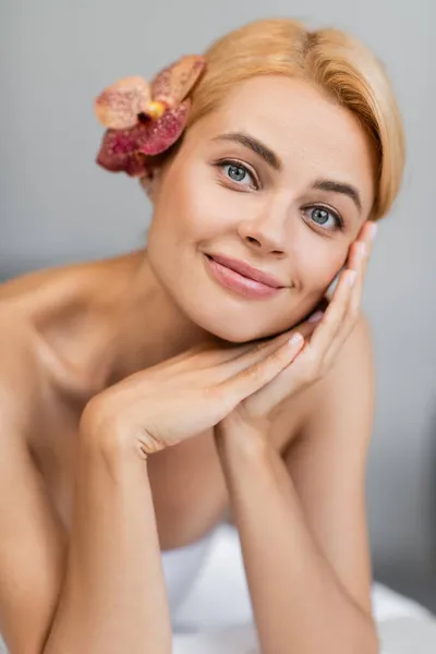 Mulher loira alegre com orquídea no cabelo sorrindo no centro de spa — Fotografia de Stock