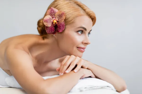 Mujer rubia complacida con orquídea en el pelo acostado en la mesa de masaje - foto de stock