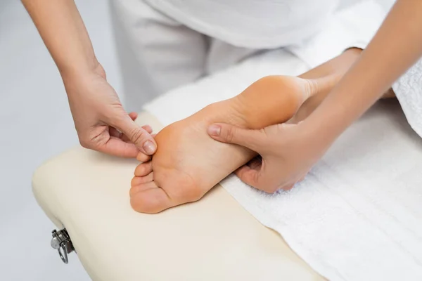 Высокий угол зрения профессионального массажиста, делающего массаж ног клиенту в спа-центре — стоковое фото