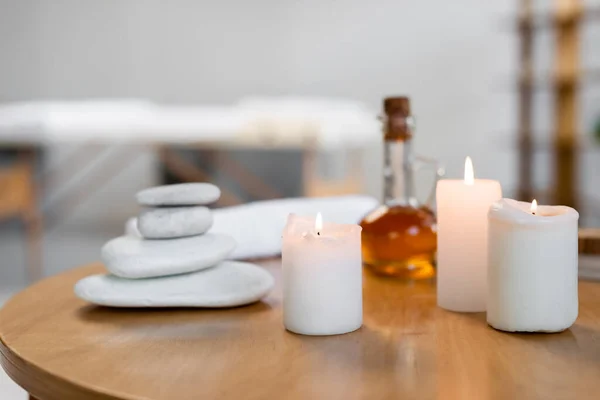 Pietre calde vicino alla brocca con olio per massaggi, candele, rotolo di asciugamani e contenitore con crema cosmetica sul tavolo — Foto stock