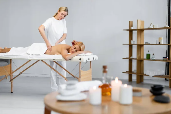 Massagista esfregando óleo de massagem na parte de trás do cliente no centro de spa com primeiro plano borrado — Fotografia de Stock