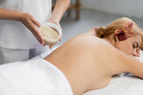 Massaggiatore contenitore di tenuta con scrub corpo vicino al cliente sul tavolo da massaggio — Foto stock