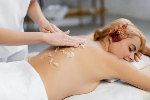 Masseur applying body scrub on back of client on massage table — Stock Photo