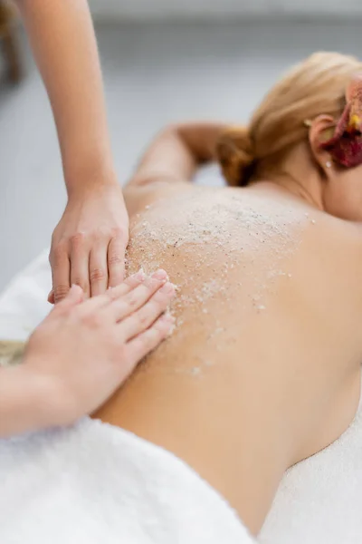 Abgeschnittene Ansicht des Masseurs, der Körperpeeling auf dem Rücken des Kunden auf dem Massagetisch anwendet — Stockfoto