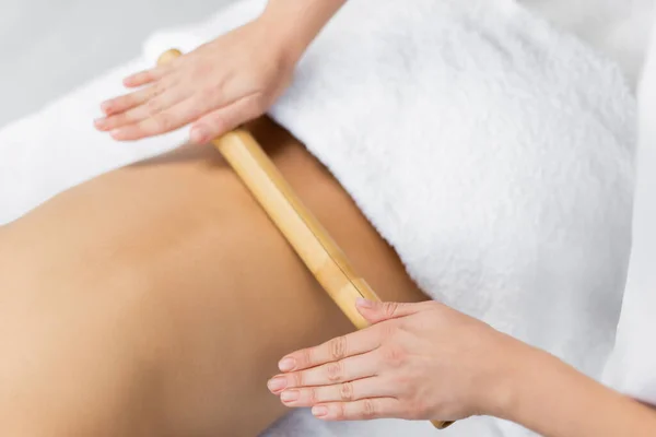 Cropped view of professional masseur massaging back of client with bamboo stick — Stock Photo