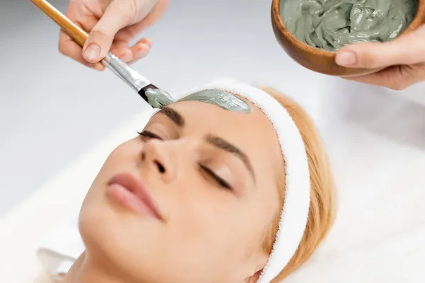 Косметолог наносить глиняну маску на обличчя жінки в спа-центрі — стокове фото