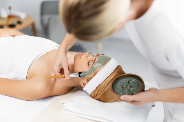 Blurred beautician applying face mask on woman in spa center — Stock Photo