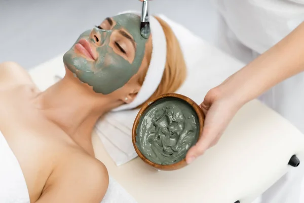 High angle view of beautician applying clay mask on face of woman lying on massage table — Stock Photo