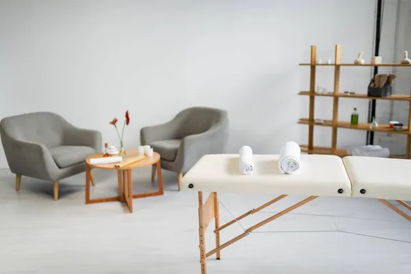 Rollos de toalla en la mesa de masaje cerca de sillones borrosos en el centro de spa - foto de stock