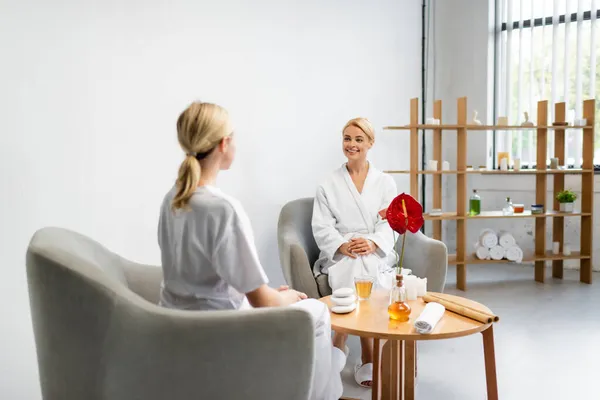 Cheerful client in bathrobe looking at blurred specialist in modern spa center — Stock Photo
