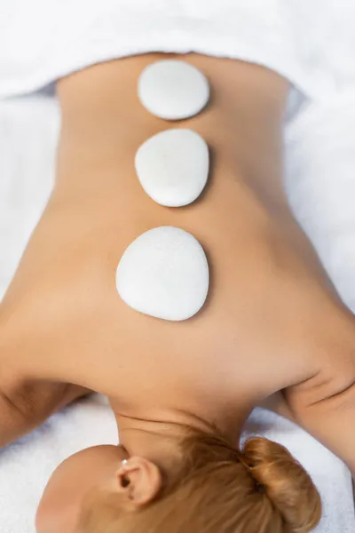 Vista dall'alto della donna bionda che riceve massaggio con pietre calde nel centro benessere — Foto stock