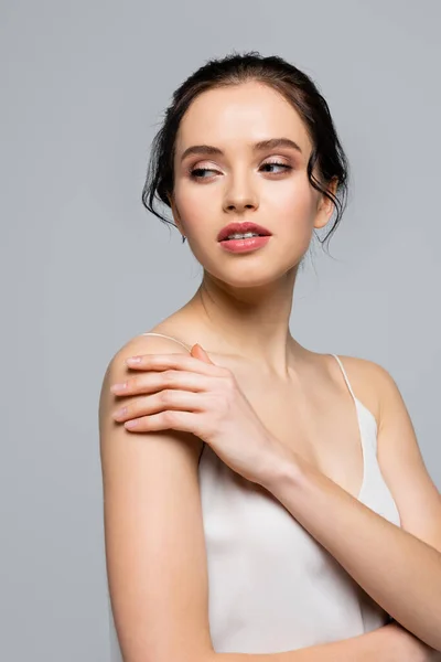 Young woman in silk dress looking away and touching shoulder isolated on grey — Stock Photo