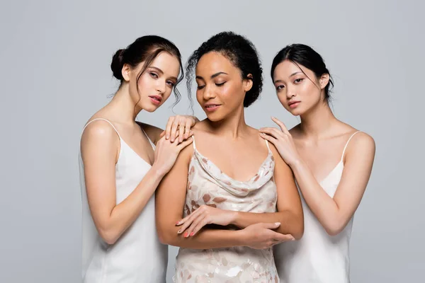 Mujeres interraciales en vestidos de satén posando aisladas sobre gris — Stock Photo