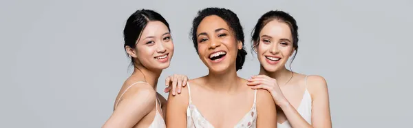 Fröhliche multikulturelle Frauen, die vereinzelt auf grauem Banner in die Kamera blicken — Stockfoto